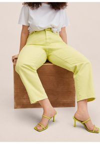 Pantalones de tiro alto amarillos claros con un corte recto, combinados con sandalias de tacón verde con tiras y una camiseta blanca atada.