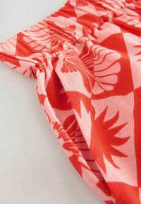 Tessuto con motivo rosso e rosa a disegni floreali, presenta una vita elastica arricciata e una texture morbida, angolato per una vista dettagliata.