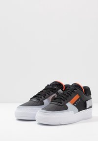 Svart och grå sneaker med en texturerad vit sula, orange detaljer och en syntetisk ovandel. Har perforeringar och en vadderad krage.