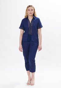 Camicia di lino navy a maniche corte con dettagli ritagliati decorativi, abbinata a pantaloni corti coordinati. Tessuto semplice e strutturato su tutta la superficie.