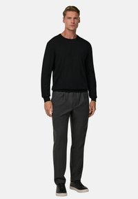 Juodas lengvas megztinis su ilgomis rankovėmis, derinamas su pilkais, laisvo kirpimo kelnėmis. Modelis dėvi juodus sportinius batelius. Paprastas, švarus dizainas.