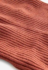 Textureret strikket stof med vandret ribbing i en varm terracotta farve, der har blødt og fleksibelt materiale.
