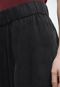 Κλείσιμο εικόνας ενός ατόμου που φοράει μαύρο παντελόνι με ελαστική μέση και κόκκινο τοπ, με το δεξί χέρι να ακουμπάει δίπλα στο παντελόνι.