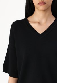 Top negro de punto con escote en V, mangas cortas y detalles acanalados. Textura suave, corte holgado y sin patrones o adornos visibles.