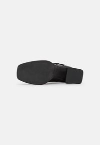 Black leather shoe with a square toe and block heel. The sole is textured rubber, featuring a minimal design and marked size.