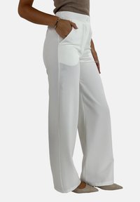 Pantalons larges blancs en tissu lisse, dotés de poches avant et d'une taille ajustée. Le vêtement présente un design épuré et minimaliste.