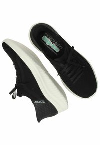 Zapatillas negras slip-on de Skechers que cuentan con una parte superior de malla transpirable, suela exterior de goma blanca gruesa y plantilla de espuma con memoria para mayor comodidad.