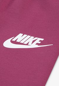 Un tissu magenta au toucher lisse présente un logo Nike blanc bien visible, écrit dans une police incurvée, positionné en diagonale sur le matériau.