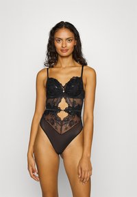 Body in lingerie nero con dettagli in pizzo floreale, pannelli in rete trasparente e coppe imbottite. Spalline regolabili e aperture laterali alte.