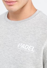 Grå bomulds sweatshirt med rund hals, med hvidt broderet tekst "PADEL CROWN CHAMPIONSHIP" på venstre brystområde.