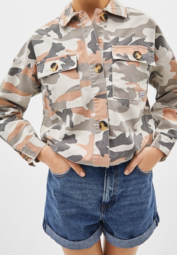 Camicia a motivo camouflage in tonalità beige, grigio e pesco, dotata di due tasche sul petto e bottoni rotondi, abbinata a pantaloni shorts in denim.