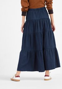 Gonna maxi blu navy a balze con vita elasticizzata e tessuto testurizzato. Abbinata a sneakers bianche con dettagli in bordeaux.