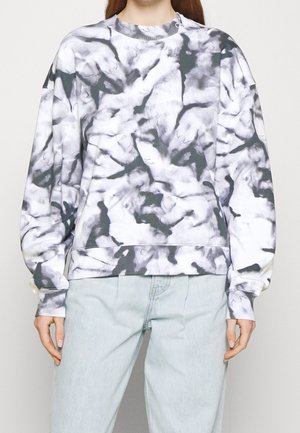 Person wearing a black and white tie-dye long sleeve sweatshirt paired with light blue jeans, standing against a plain background.