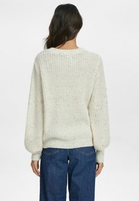Cremfarbener, gestrickter Pullover in lässiger Passform, mit geripptem Saum und Bündchen. Mehrfarbige Flekken im Stoff verleihen dem Kleidungsstück Details.
