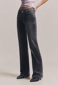 Blugi evazați negri din denim cu talie înaltă, ușor decolorați și cu design cu cinci buzunare. Asortați cu pantofi negri cu vârf ascuțit.