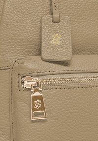 Bolso de cuero texturizado beige con cremallera dorada y etiqueta a juego grabada con las iniciales "ZZ" y "EST. 2007" en letras doradas.