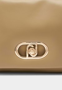 Borsa in pelle beige con una chiusura prominente color oro dal design circolare. Texture liscia e stile minimalista che enfatizzano l'eleganza.