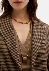 Collana dorata con catena a maglie e un pendente che presenta una pietra marrone lucida. Blazer notevole con motivo houndstooth in toni neutri.