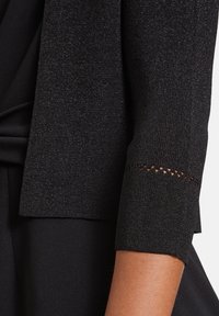 Fekete bordázott kardigán strukturált anyagból és fémszállal. Háromnegyed hosszú ujjakkal rendelkezik, a mandzsettán dekoratív kivágás részlettel.