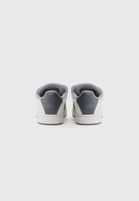 Ténis com parte superior em camurça cinzenta e bege, colarinho almofadado e sola de borracha. Apresentam um logótipo no calcanhar e detalhes em costura.