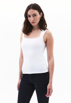 White fitted tank top with a square neckline, made of smooth fabric. Paired with dark, slim-fit jeans.
