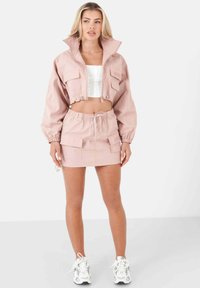 Avskuren ljusrosa jacka med två framfickor och matchande minikjol med fickor. Vit topp och tjocka vita sneakers kompletterar outfiten.