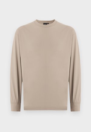 Chemise beige à manches longues avec col rond et poignets élastiqués, design simple, sans motifs ni logos visibles sur fond blanc.