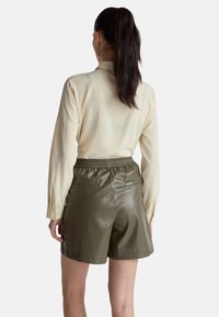 Jedwabna bluzka w kremowym kolorze z kołnierzykiem i długimi rękawami, zestawiona z oliwkowozielonymi szortami ze sztucznej skóry z elastycznym pasem i bocznymi kieszeniami.