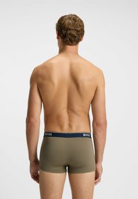 Male model seen from the back wearing olive green boxer briefs with a navy waistband labeled “BOSS” against a plain white background.