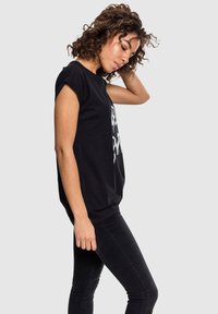Sort oversized t-shirt lavet af bomuld, med rullede ærmer og hvid grafisk print. Båret med tætsiddende sorte jeans.