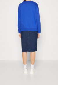 Sudadera azul con cuello redondo, combinada con una falda lápiz de mezclilla con dobladillo sin rematar. Zapatillas blancas completan el atuendo.