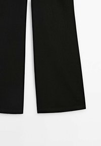 Pantalon noir à jambes larges, visible du milieu de la cuisse jusqu’à l’ourlet sur fond blanc.
