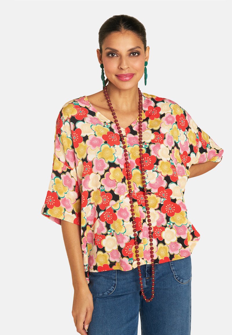 Colorful floral-patterned blouse with short sleeves. Features a V-neck and loose fit, made from lightweight fabric. Worn with denim jeans.