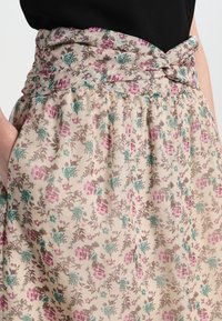 Falda floral de tela ligera con un fondo beige. Presenta rosas en tonos rosa y verde azulado con acentos verdes y una cintura anudada.