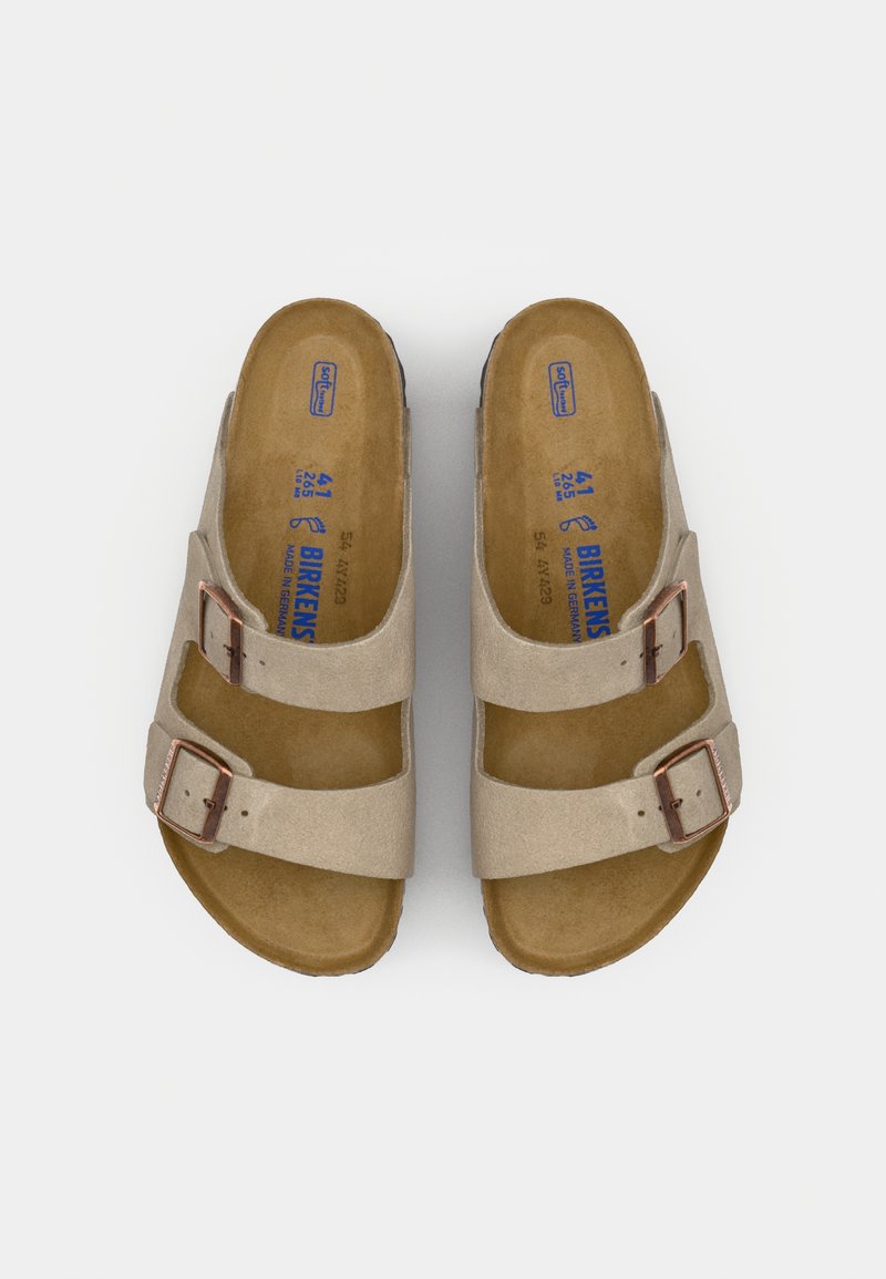 Beige suede sandals with two adjustable straps and metal buckles. Contoured cork footbed with a smooth texture and a black rubber sole.
