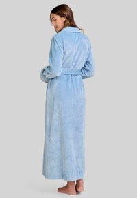 Bata de baño larga y de color azul claro, hecha de un tejido suave y con textura. Cuenta con un cuello, un cinturón y una superficie decorada con un sutil diseño en cuadrícula.