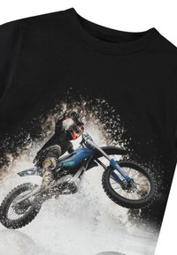 Melna T-kreklu ar grafiku, kurā attēlots braucējs uz zilā motocikla, ko ieskauj ūdens un netīrumu šļakatas, uzsverot kustību un dinamiku.