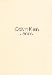 Krémové bavlněné tričko s hladkou texturou, se šedým logem "Calvin Klein Jeans" umístěným na hrudi ve moderním písmu.
