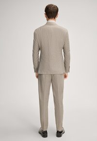 Jasnobrązowy garnitur w kratę, o dopasowanym kroju, z jednym rozcięciem i dopasowanymi spodniami. Uzupełniony błyszczącymi czarnymi butami.