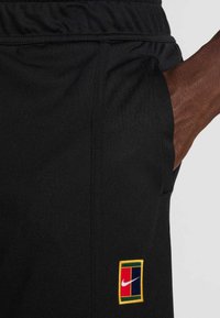 Μαύρο αθλητικό σορτς με πολύχρωμο patch του λογότυπου της Nike. Το ύφασμα φαίνεται λείο με ελαστική μέση και πλαϊνές τσέπες.