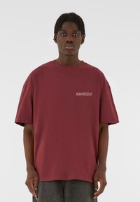 Maroon oversized t-shirt made from cotton. Features a crewneck design and subtle logo in gray on the chest. Short sleeves with relaxed fit.