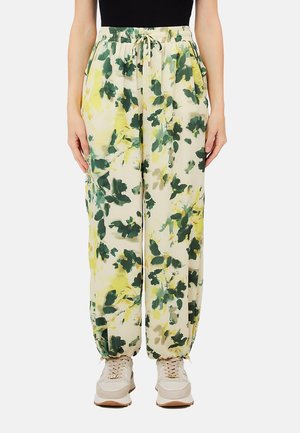 Pantaloni a vestibilità comoda con stampa di foglie verdi e gialle, vita elasticizzata con coulisse e polsini elasticizzati, indossati con sneakers beige.