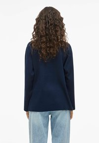 Pull bleu marine avec une texture côtelée, doté de manches longues et d'une coupe ample, associé à un jean taille haute, de couleur bleue claire.