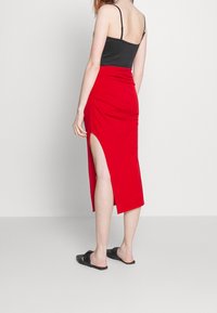 Roter, knielanger Rock mit seitlichem Schlitz und gerafftem Design, kombiniert mit einem schwarzen Tanktop und schwarzen Riemchensandalen. Minimalistische Ästhetik.
