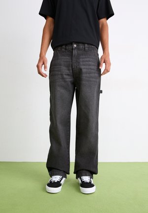 Black denim jeans with a straight cut, slight fading at the thighs, five-pocket design, and a side patch pocket, worn with black sneakers.