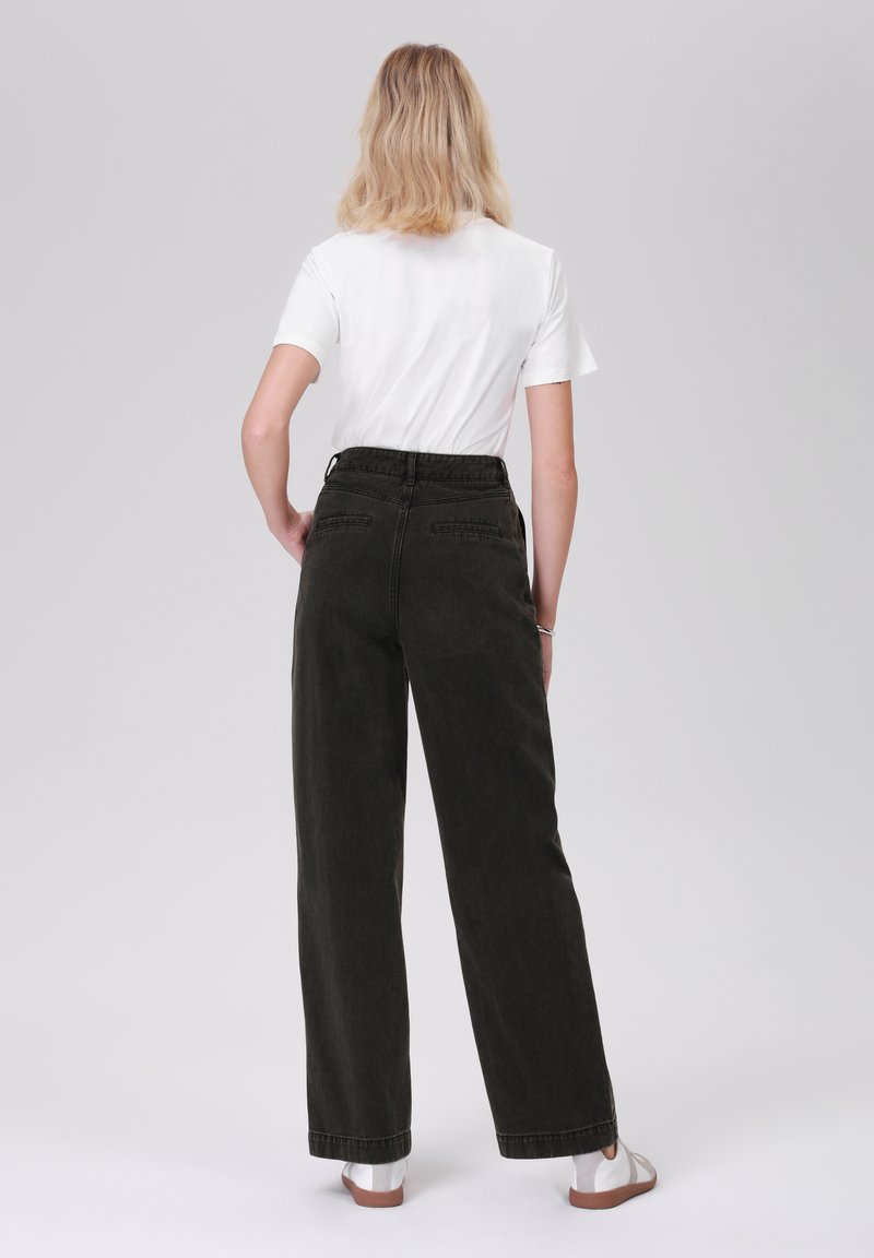 Donkergroene jeans met wijde pijpen en hoge taille, voorzien van achterzakken en een soepele textuur, gecombineerd met een eenvoudig wit T-shirt.