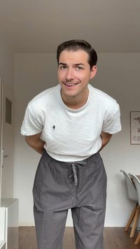 Vit T-shirt med kort ärm och liten broderad logotyp, parat med löst sittande grå byxor med elastisk midja och dragsko.