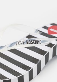 Infradito in plastica trasparente con suola a righe bianche e nere, superficie testurizzata e "LOVE MOSCHINO" stampato sulla fascia.