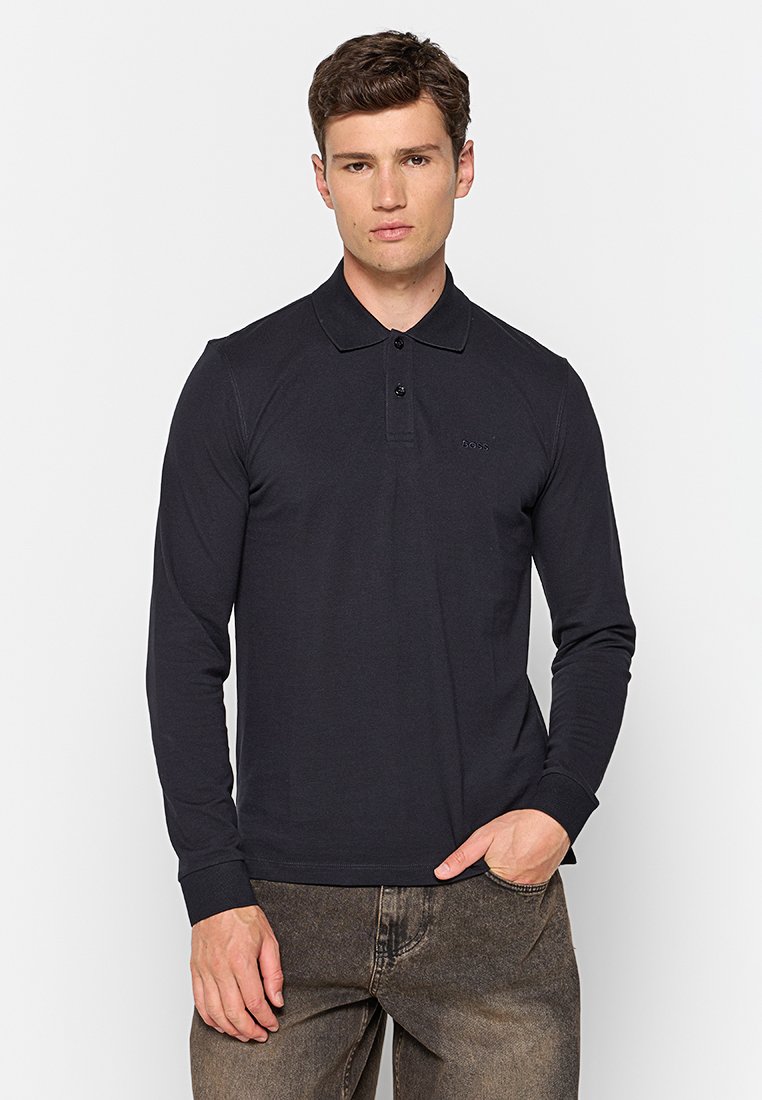 Zwarte langemouwen polo met een kraag en een drie-knopens sluiting, met een klein logo op de borst en geribbelde manchetten, gecombineerd met een donkere broek.