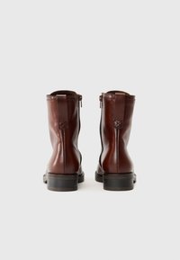 Bottines en cuir marron avec une finition lisse, fermeture éclair et languette à l'arrière. Talon carré et détails de design minimalistes.
